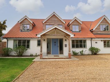 A house with a red tiled roof and blue front door with gravel driveway and grass at Little Chapter in Walberswick