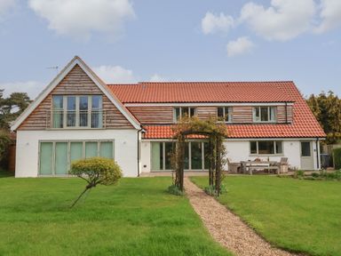 A large house with a red tiled roof and wooden cladding with a garden path leading to a wooden arch at Little Chapter in Walberswick