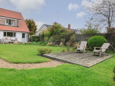 A garden with grass lawn wooden patio chairs and a gravel path near a house at Little Chapter in Walberswick