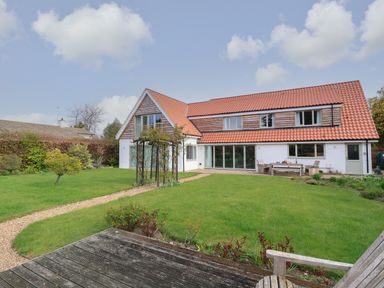 A garden with a wooden table and chairs green lawn and a house with red roof tiles and wooden cladding at Little Chapter in Walberswick
