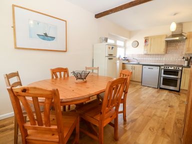 A kitchen with wooden dining table and chairs a refrigerator stove dishwasher and cabinets at Jacuma in Rhosneigr