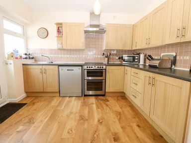 A kitchen with wooden cabinets a dishwasher stove microwave and wooden floor at Jacuma in Rhosneigr