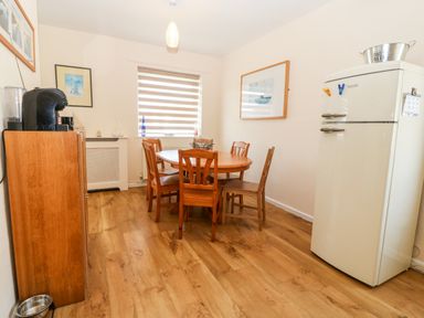 A dining area with a round wooden table and five chairs wooden cabinet with coffee machine and fridge in a room at Jacuma in Rhosneigr