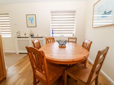 A dining room with a wooden table and six chairs near windows with blinds and nautical decorations at Jacuma in Rhosneigr