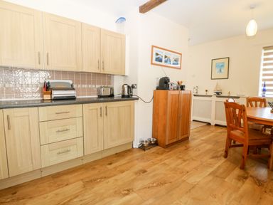 A kitchen and dining area with wooden cabinets small appliances a wooden dining table and chairs and framed pictures on the walls at Jacuma in Rhosneigr