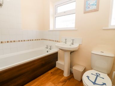 A bathroom with a bathtub a pedestal sink a toilet with an anchor design and a small waste bin at Jacuma in Rhosneigr