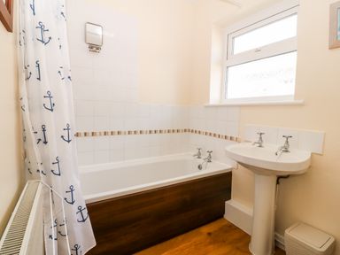 A bathroom with a bathtub a shower curtain a sink a window and a radiator at Jacuma in Rhosneigr