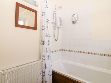 A bathroom with a bathtub shower combination nautical shower curtain and a mirror above a radiator at Jacuma in Rhosneigr
