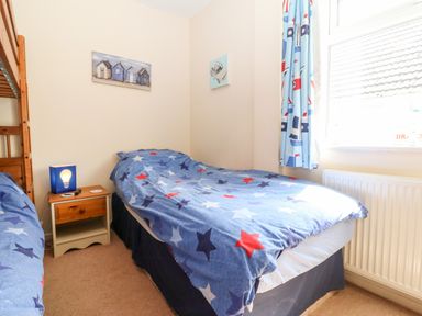 A bedroom with two single beds a wooden nightstand and a window with blue curtains at Jacuma in Rhosneigr