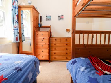 A bedroom with bunk beds blue star patterned bedding wooden wardrobes and dressers at Jacuma in Rhosneigr