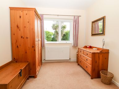 A bedroom with wooden wardrobe wooden chest wooden dresser and a window with striped curtains at Jacuma in Rhosneigr