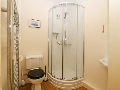 A bathroom with a corner shower enclosure toilet with black seat and a small white sink at Jacuma in Rhosneigr