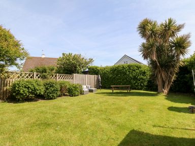 A backyard with grass lawn a wooden fence bushes outdoor seating table and umbrella Jacuma in Rhosneigr