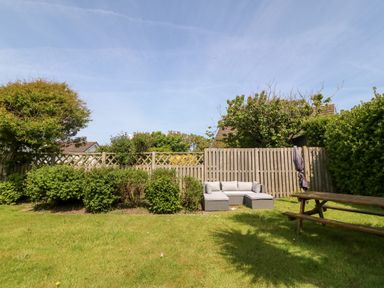 A garden with a wooden fence bushes a grey outdoor sofa and a picnic table at Jacuma in Rhosneigr