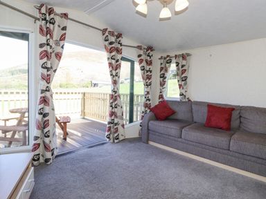 A living room with a gray sofa and red cushions near sliding glass doors with patterned curtains overlooking a wooden deck at Swinside in Lorton