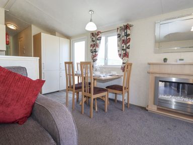 A dining area with a wooden table and four chairs near a window with patterned curtains and a fireplace in the corner at Swinside in Lorton