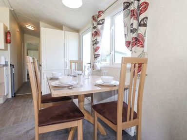 A dining area with a wooden table set for four including plates bowls glasses and cutlery next to a window with patterned curtains at Swinside in Lorton