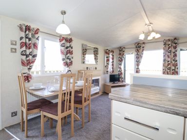 A dining area with a table set for four next to a window with patterned curtains and a living area with a fireplace and television at Swinside in Lorton