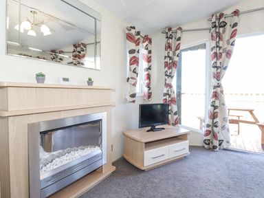 A living room with a modern fireplace a small tv on a wooden stand patterned curtains and a glass door leading outside at Swinside in Lorton
