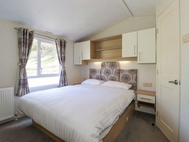 A bedroom with a double bed white bedding headboard with flower pattern curtains and built in cabinets at Swinside in Lorton