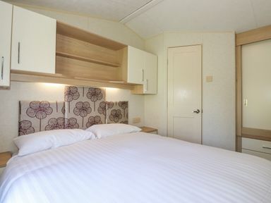 A bedroom with a bed white pillows floral headboard wall cabinets and a door at Swinside in Lorton