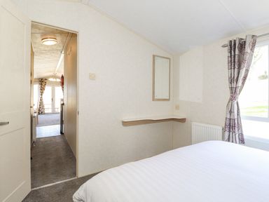 A bedroom with a bed a wall mirror a small shelf and a window with patterned curtains at Swinside in Lorton