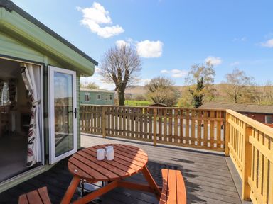 A wooden deck with a round picnic table and three mugs outside a green mobile home at Swinside in Lorton