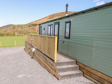 A green mobile home with wooden steps and railing on a gravel area with hills in the background at Swinside in Lorton