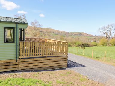 A gravel driveway next to a fenced grassy area with a caravan and wooden deck overlooking hills at Swinside in Lorton