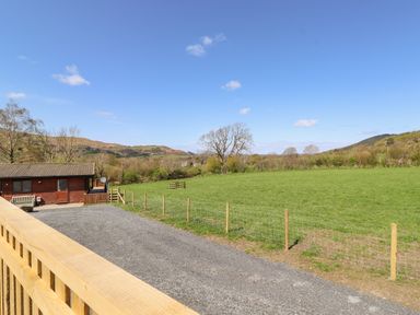 A fenced gravel driveway next to a wooden building and a green field with hills in the background at Swinside in Lorton