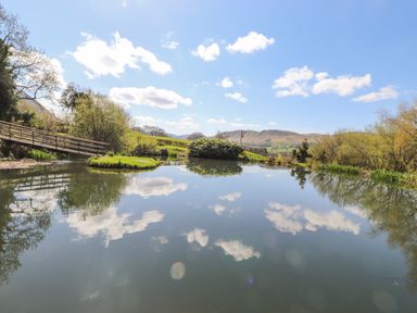 A pond with a small island and a wooden footbridge surrounded by trees and hills at Swinside in Lorton