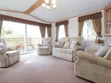 A living room with beige sofas and armchairs near large windows with brown curtains at Whiteside in Lorton