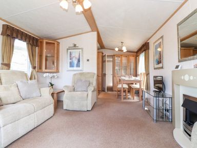 A living room with beige sofas a glass TV stand a dining table with chairs and a fireplace at Whiteside in Lorton