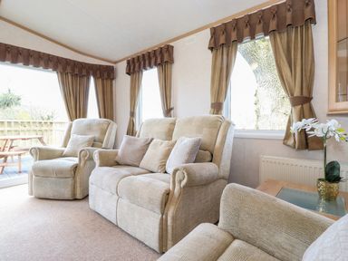A sitting room with beige sofas and armchairs next to windows with brown curtains and a small table with a plant at Whiteside in Lorton