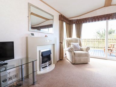 A living room with a beige armchair near a glass sliding door a fireplace with a mirror above it and a glass TV stand with a TV at Whiteside in Lorton