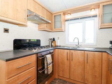 A kitchen with wooden cabinets a gas stove an oven a sink under a window and kitchen utensils at Whiteside in Lorton