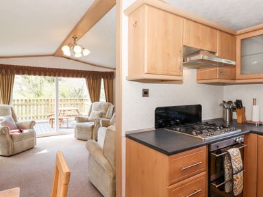 A kitchen with wooden cabinets and a gas stove next to a living area with armchairs and sliding glass doors leading to a deck at Whiteside in Lorton
