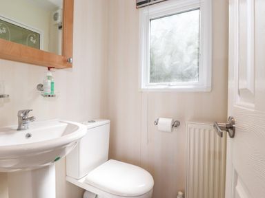 A small bathroom with a sink toilet wall-mounted soap dispenser mirror window and radiator at Whiteside in Lorton