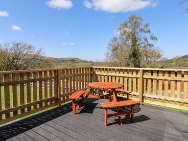 An outdoor wooden deck with a round picnic table and benches surrounded by a wooden fence with hills in the background at Whiteside in Lorton