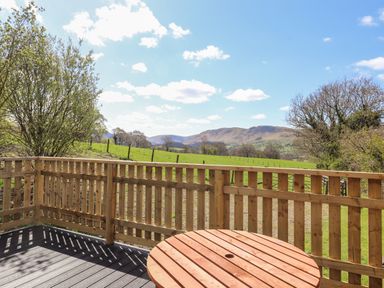 A wooden deck with a round wooden table overlooking green fields and hills at Whiteside in Lorton
