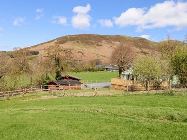 A fenced grassy field with wooden sheds and a small house with a deck near hills at Whiteside in Lorton
