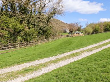 A gravel pathway through a grassy field with a wooden fence and trees leading to buildings at Whiteside in Lorton