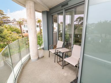 A balcony with two chairs and a small table overlooking trees and buildings at Sebastians View in Falmouth
