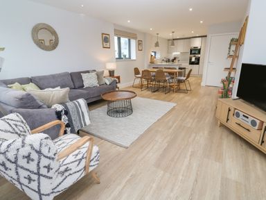 An open plan living room and kitchen with a grey sofa an armchair and a dining table at Sebastian's View in Falmouth