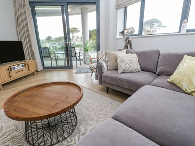 A living room with a grey sofa coffee table television and sliding glass door leading to a balcony at Sebastian's View in Falmouth