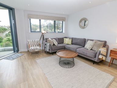 A living room with a grey sectional sofa pillows and blankets a round wooden coffee table an armchair a floor lamp a rug a round wall mirror and a window at Sebastian's View in Falmouth