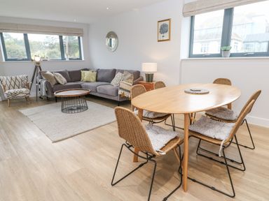 A living room with a gray sofa a wooden oval dining table with chairs and large windows at Sebastian's View in Falmouth