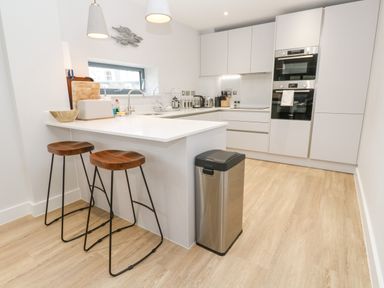 A kitchen with white cabinets two wooden stools and stainless steel appliances at Sebastians View in Falmouth