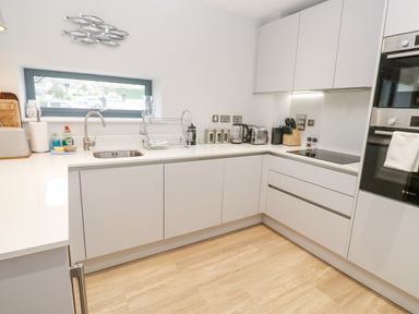 A modern kitchen with white cabinets a sink a toaster kettle and built in oven at Sebastians View in Falmouth