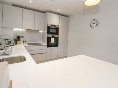 A modern kitchen with white cabinets a double oven a sink and a wall clock at Sebastian's View in Falmouth